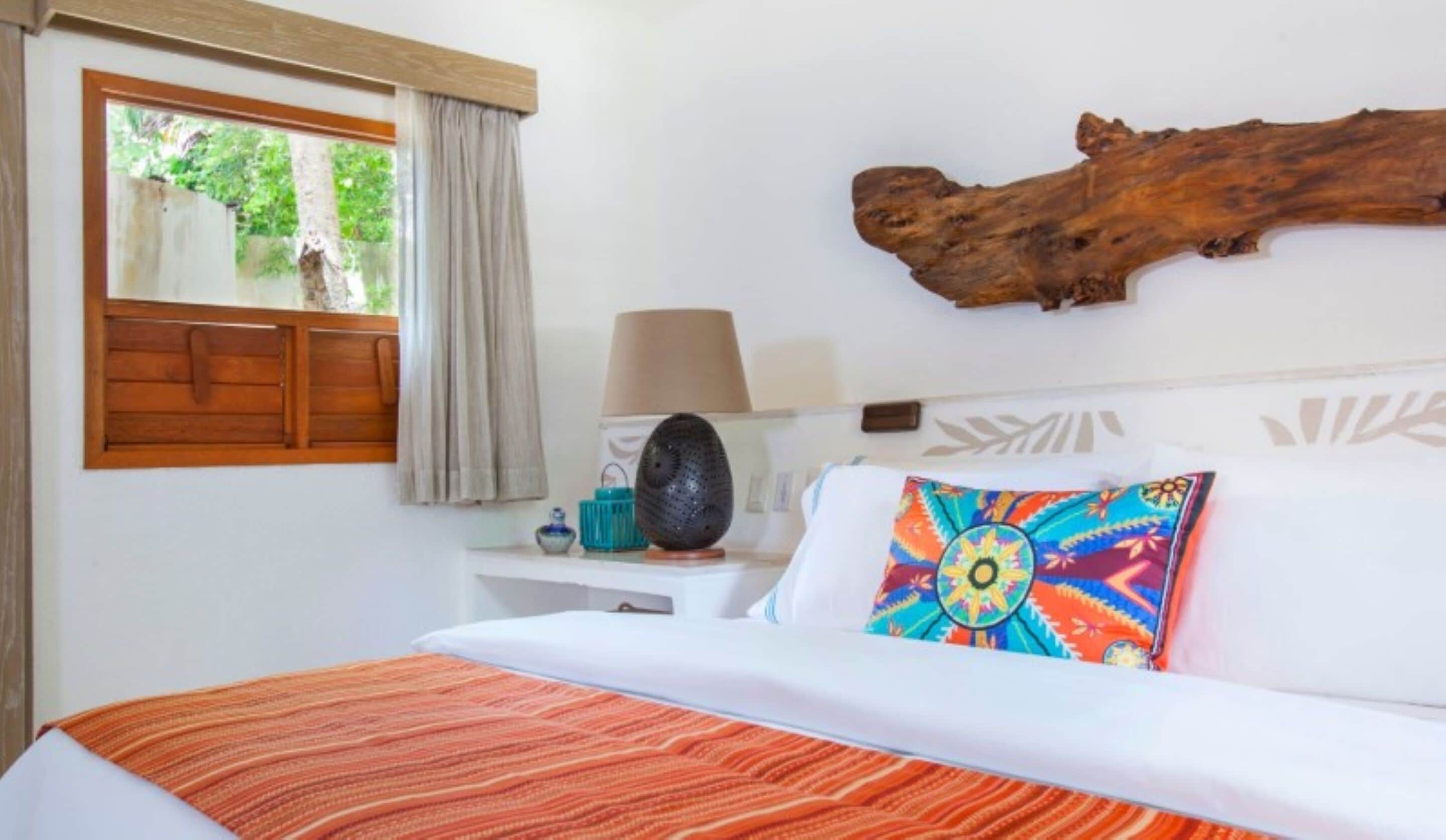 A bedroom with a bed, a window with curtains, a nightstand with a lamp, and a decorative piece on the wall.