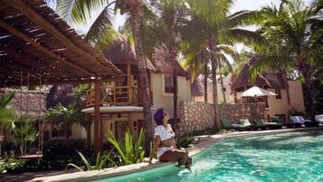 A poolside area with a thatched roof, palm trees, and a pool.