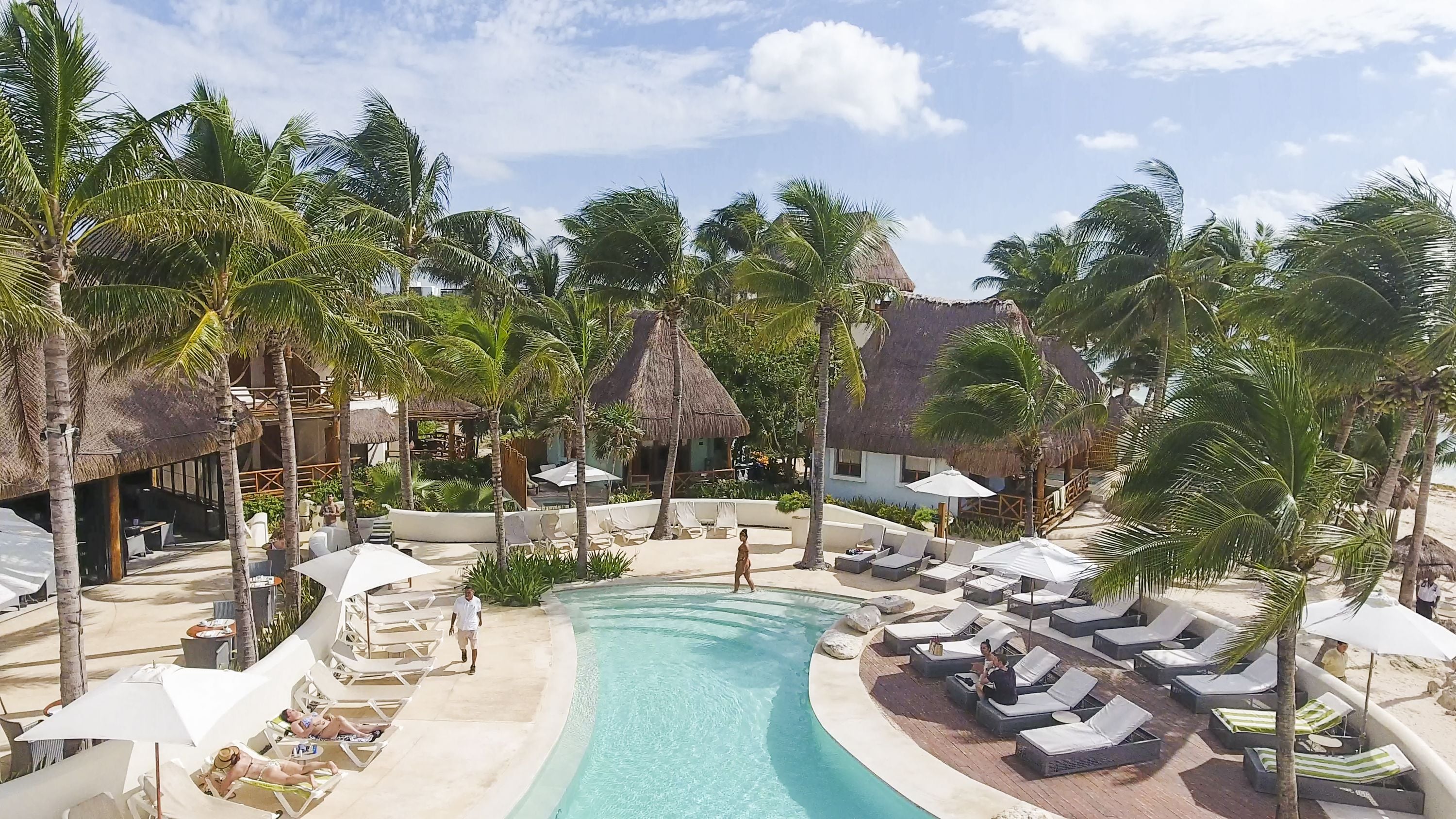 Un espace piscine aménagé dans un complexe hôtelier, avec des chaises longues, des parasols et des palmiers.