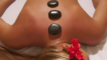 A person receiving a back massage with heated stones placed along the spine.