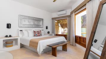 A bedroom with a bed, bedside tables, a bench, a ceiling fan, and a large window with curtains.