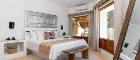 A bedroom with a bed, bedside tables, a bench, a ceiling fan, and a large window with curtains.