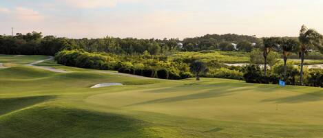 A golf course with a flag, trees, and a distant building.