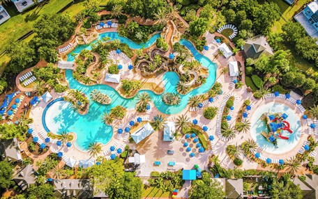 Vue aérienne d’un complexe hôtelier doté de plusieurs piscines, d’espaces de détente et de palmiers.