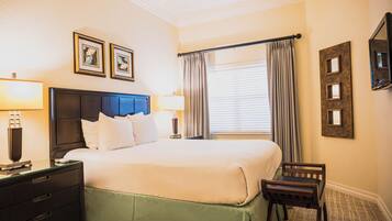 Una habitación de hotel con una cama, dos lámparas de noche, una mesita de noche, una silla, una ventana con cortinas y cuadros en la pared.