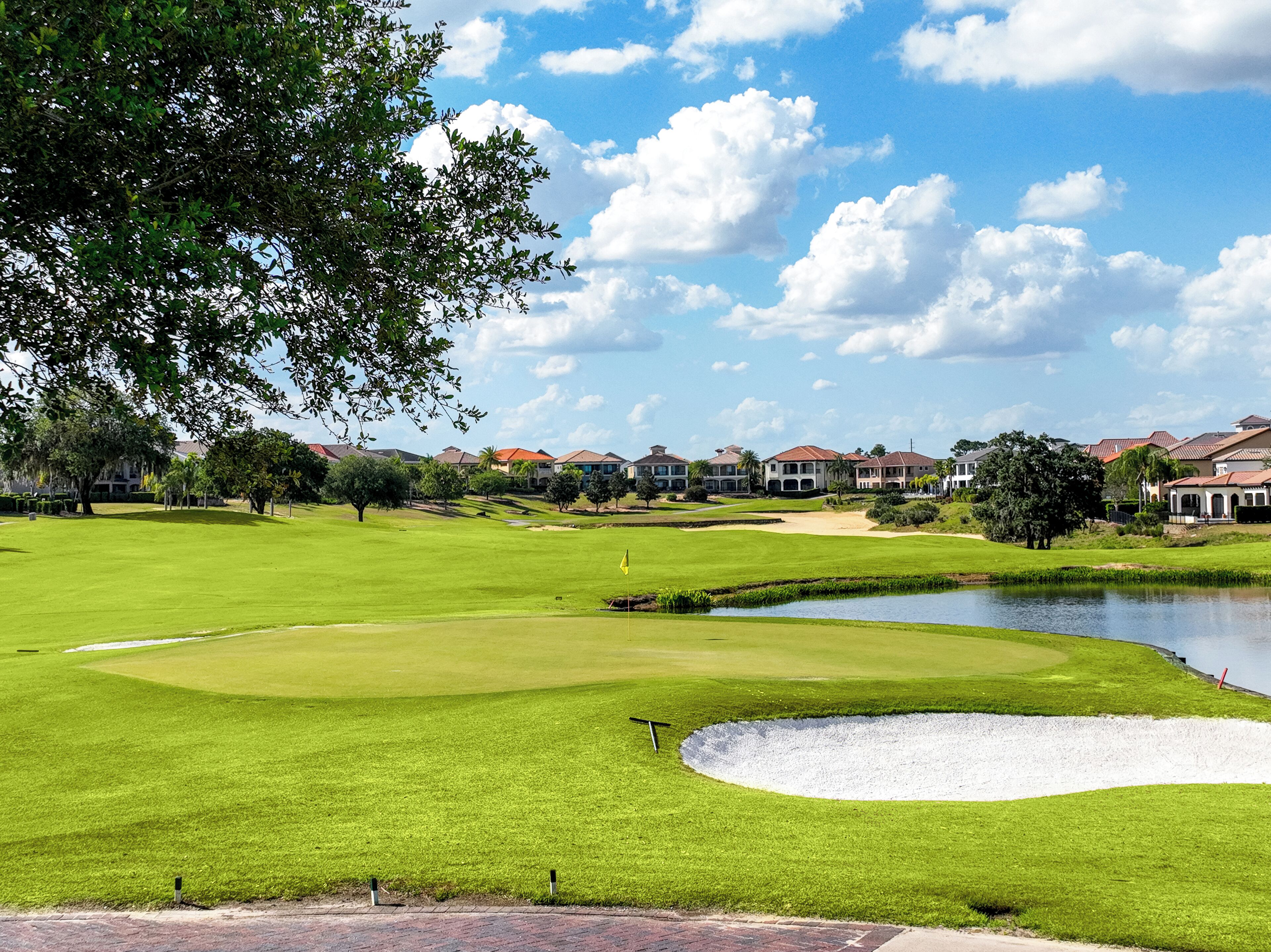 A golf course with a pond, sand bunkers, and houses in the background.