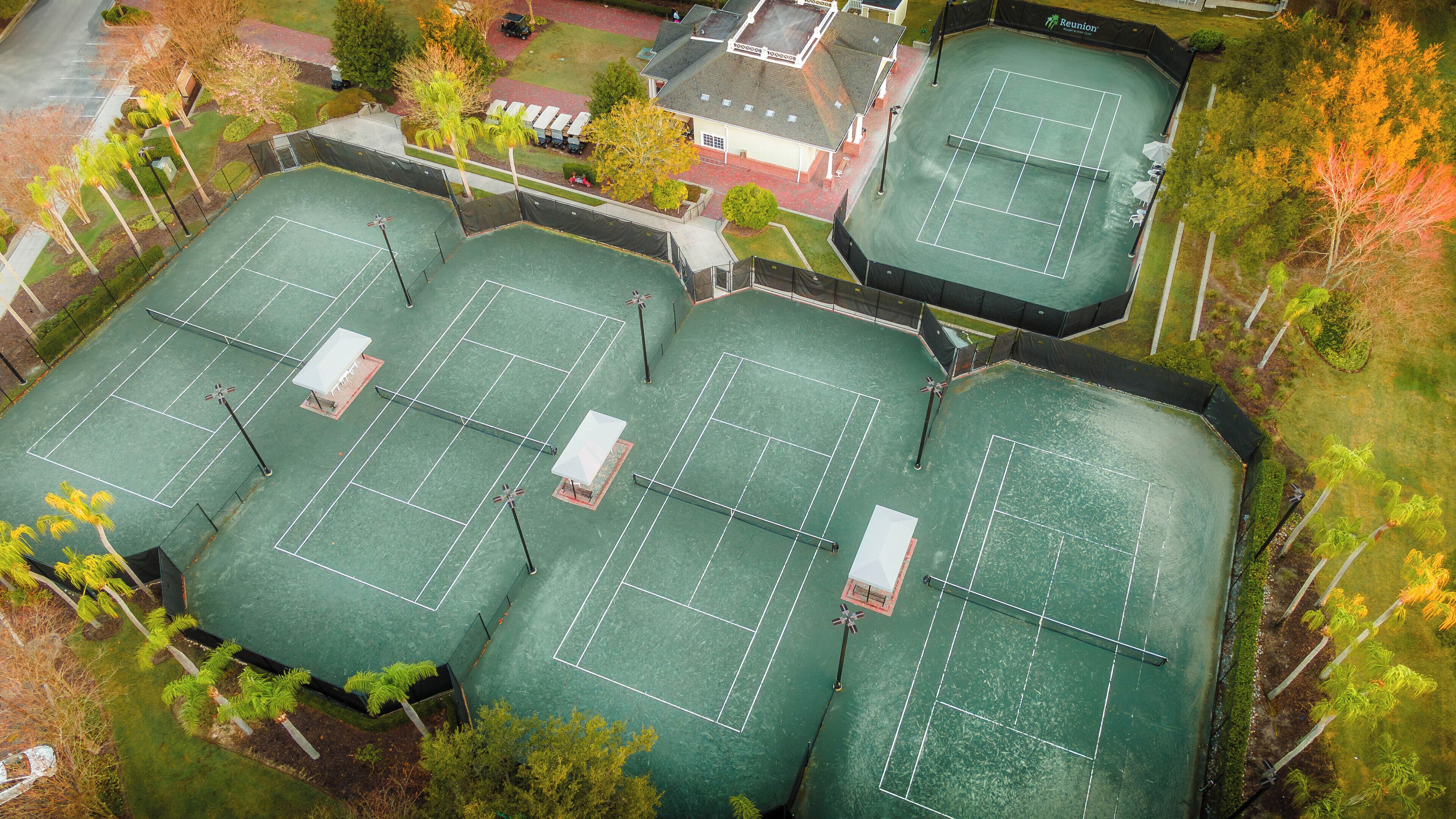 Ilmakuva tenniskeskuksesta, jossa on useita kenttiä, ja jonka ympärillä on puita ja rakennus, jonka kyltissä lukee ”Reunion”.