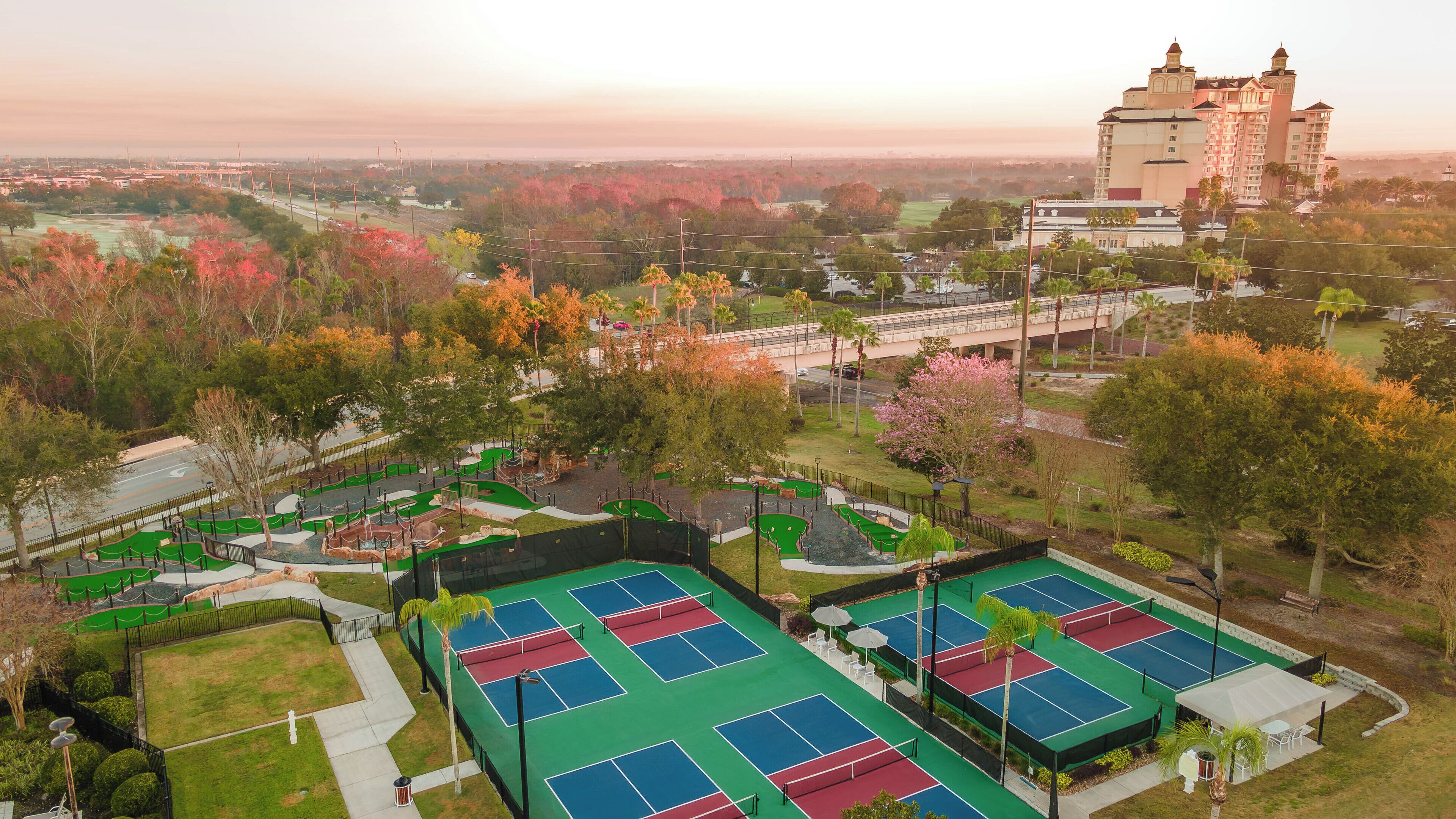A tennis court complex with multiple courts, surrounded by trees and a castle-like building in the background.