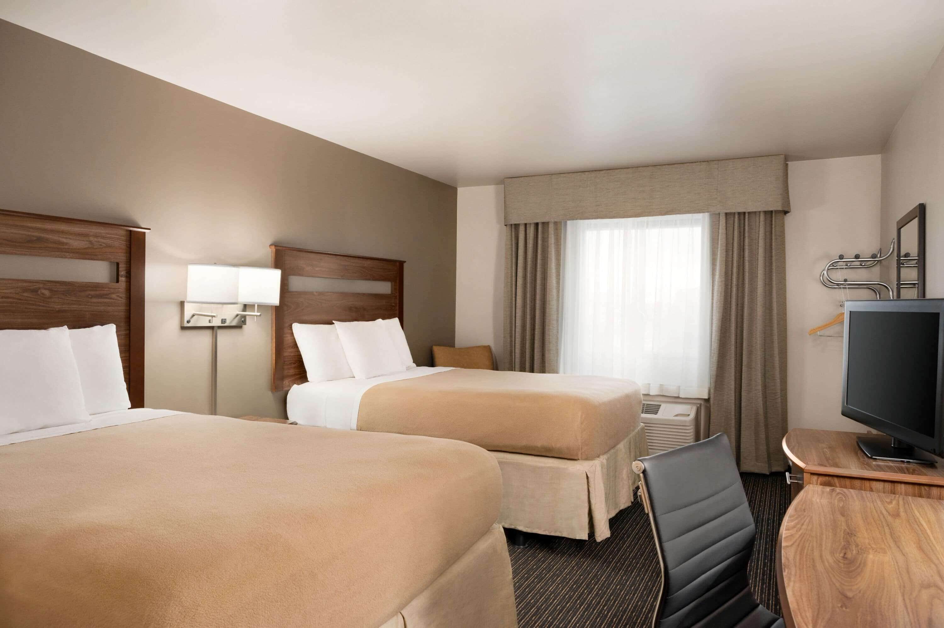 A hotel room with two beds, a desk with a television, and a window with curtains.