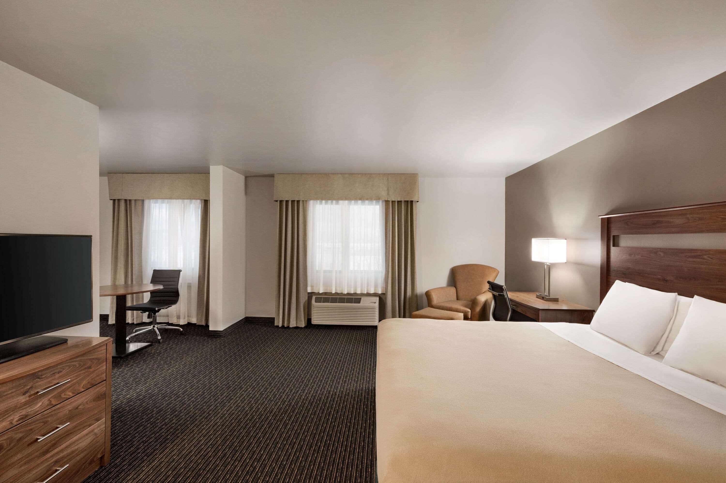 A hotel room with a large bed, a desk with a chair, a television, and a lamp.