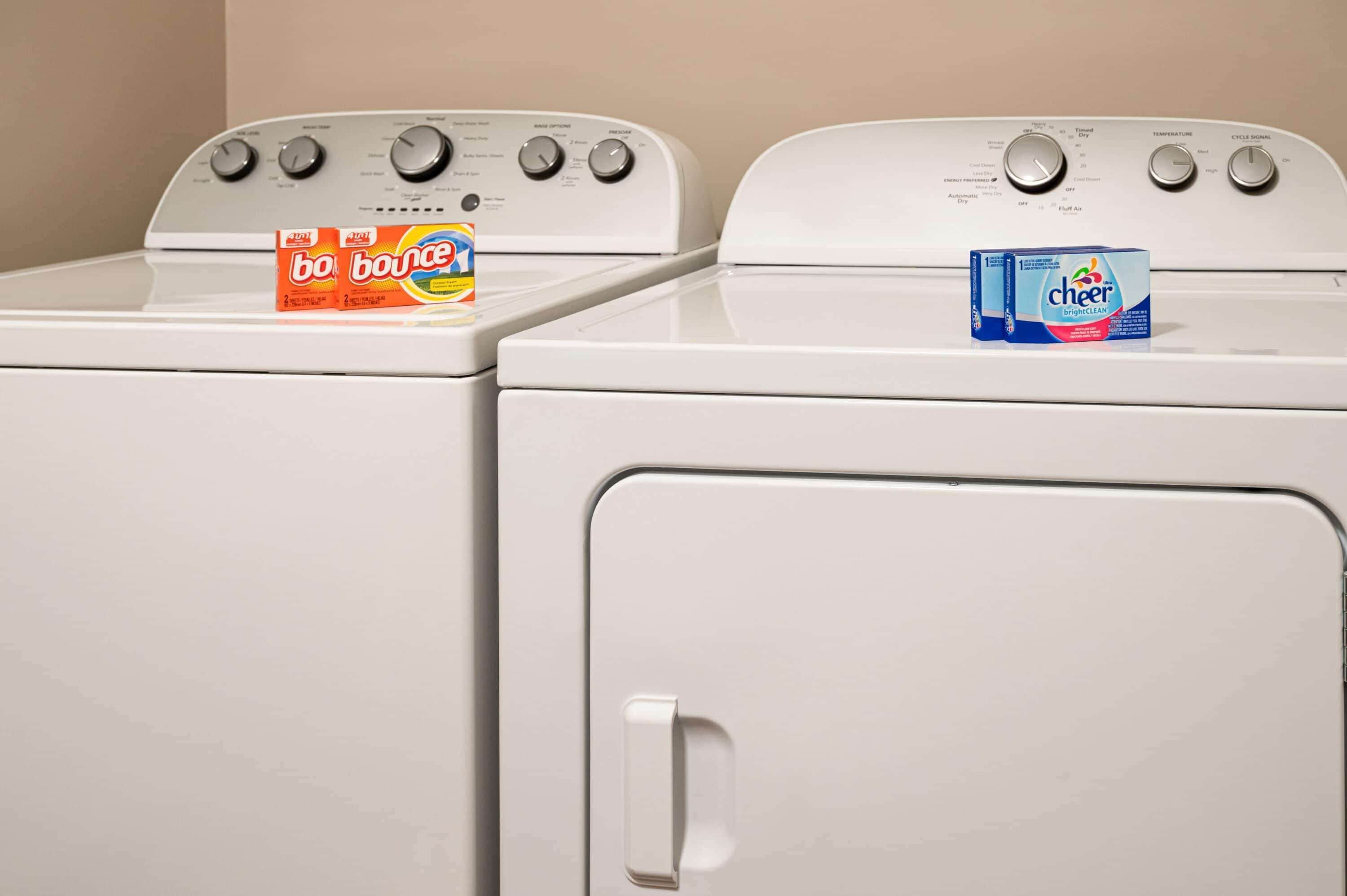 Two white washing machines with detergent boxes on top.