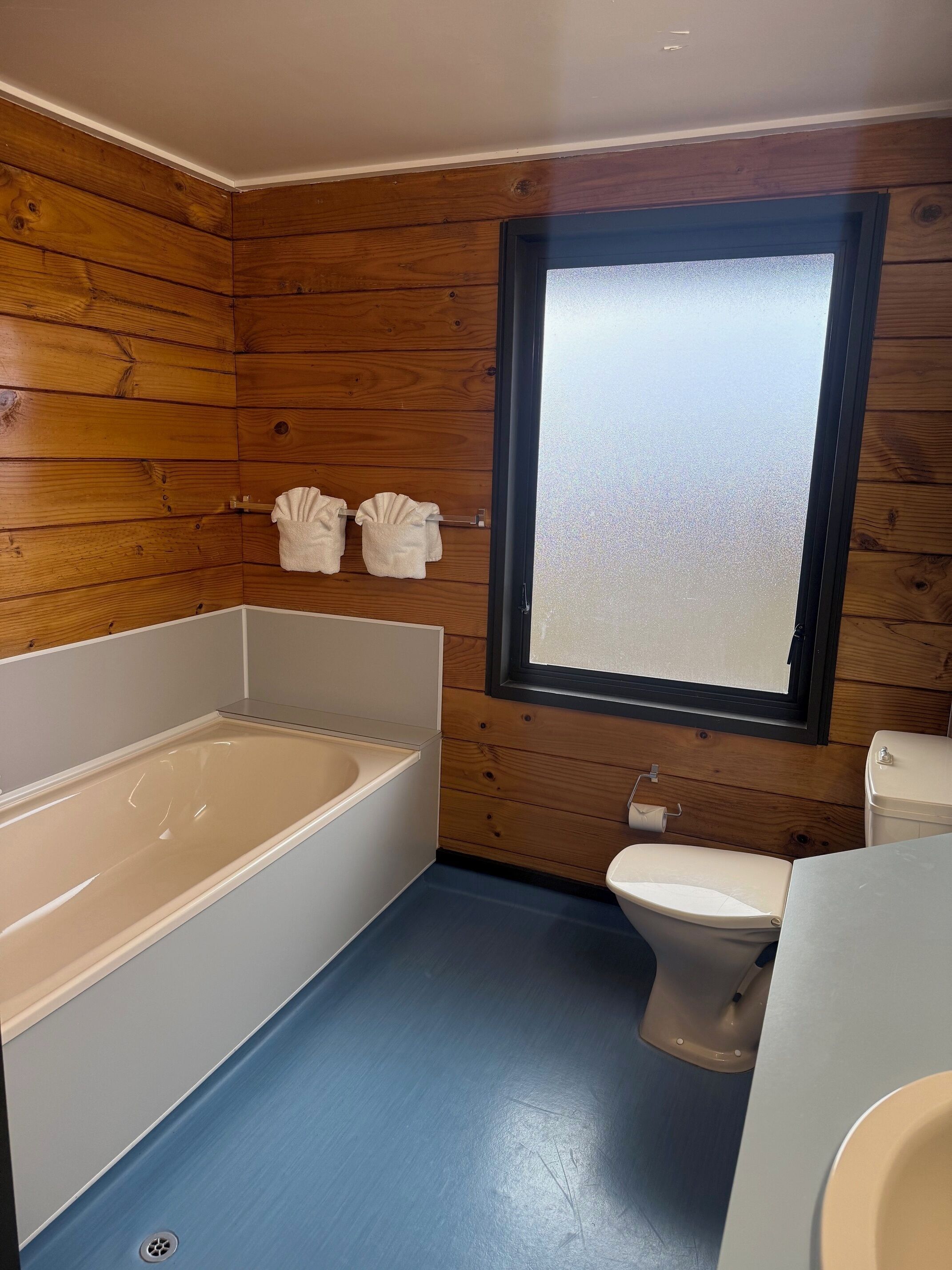 Un baño con paneles de madera, una bañera, un inodoro y una ventana.
