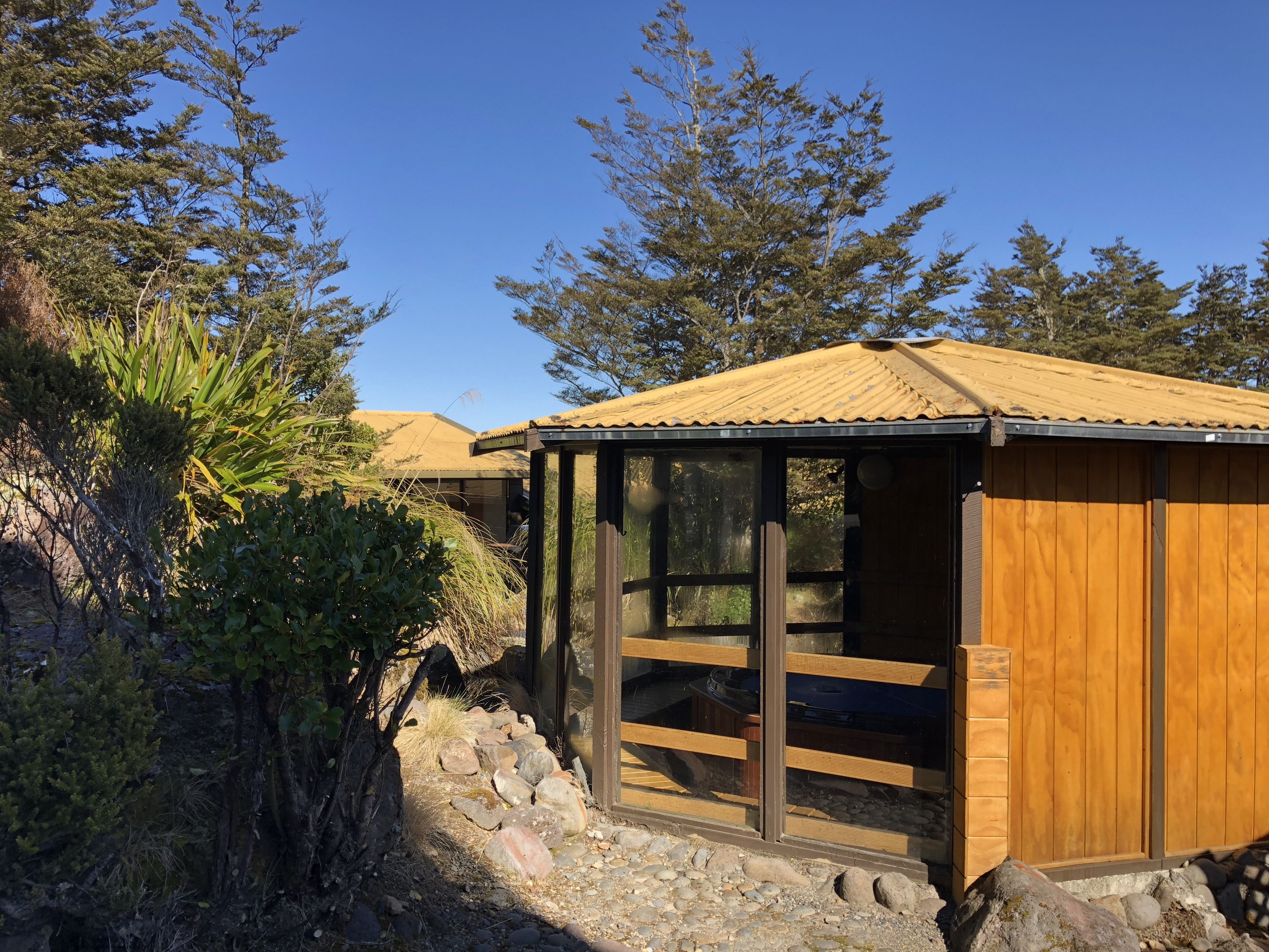 A wooden cabin with a metal roof, surrounded by natural vegetation and trees.
