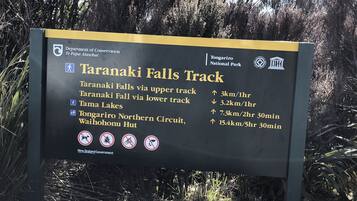 Señal del sendero Taranaki Falls con indicaciones y distancias a varios puntos de interés.