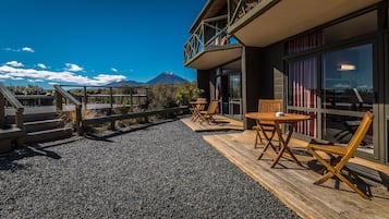 A wooden deck with outdoor seating, a mountain view, and a building with large windows.