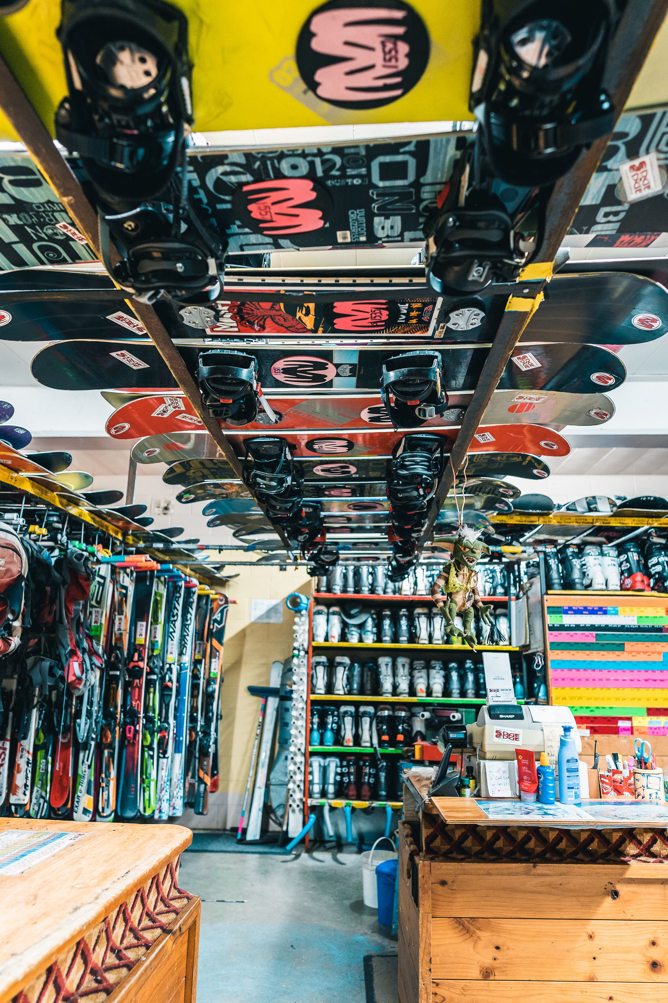 Tienda de esquí con varios esquíes y tablas de snowboard colgados del techo, un mostrador de madera y estantes llenos de equipo de esquí.