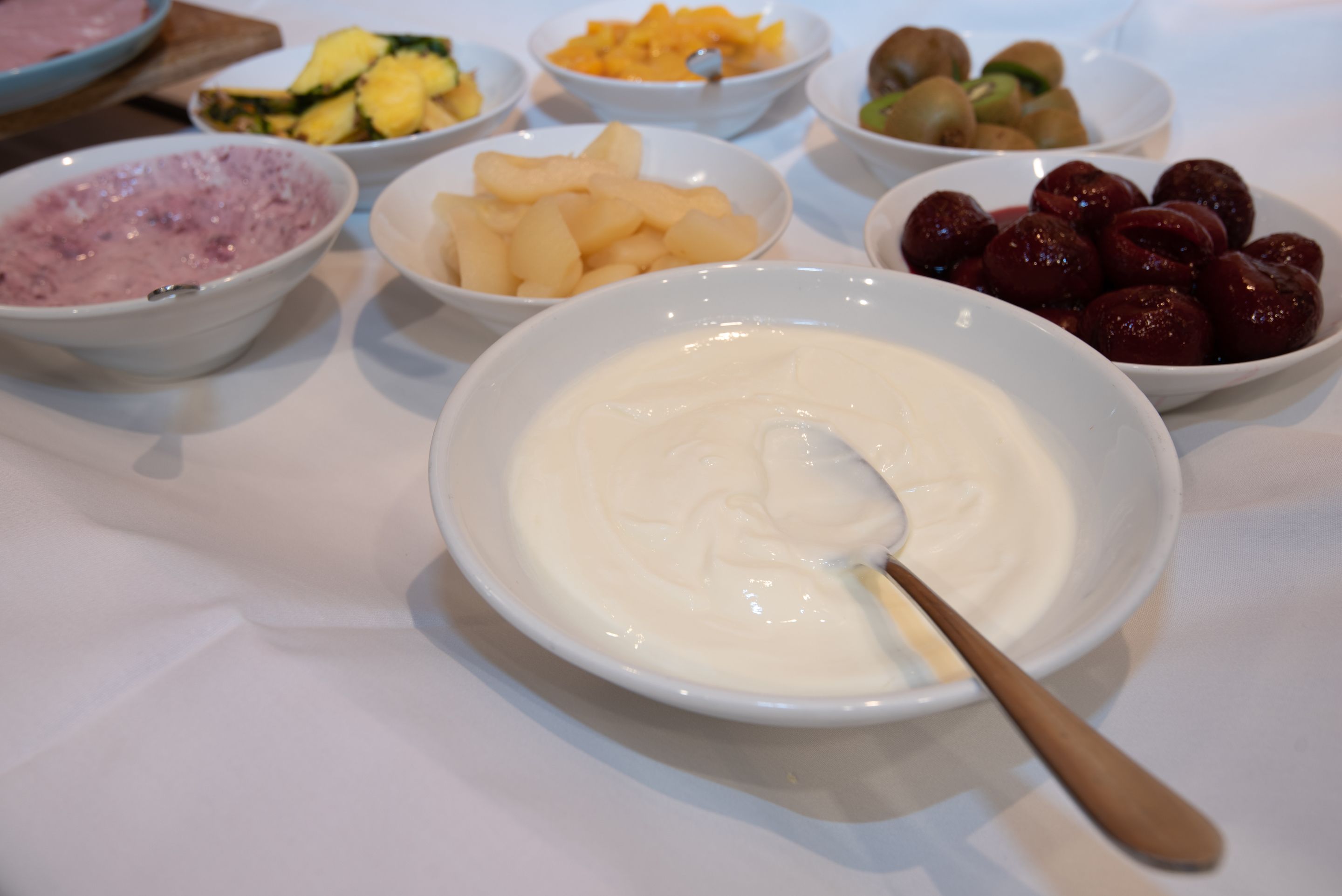 Ein Tisch mit verschiedenen Schalen voller Speisen, darunter Obst und eine Schale Joghurt.