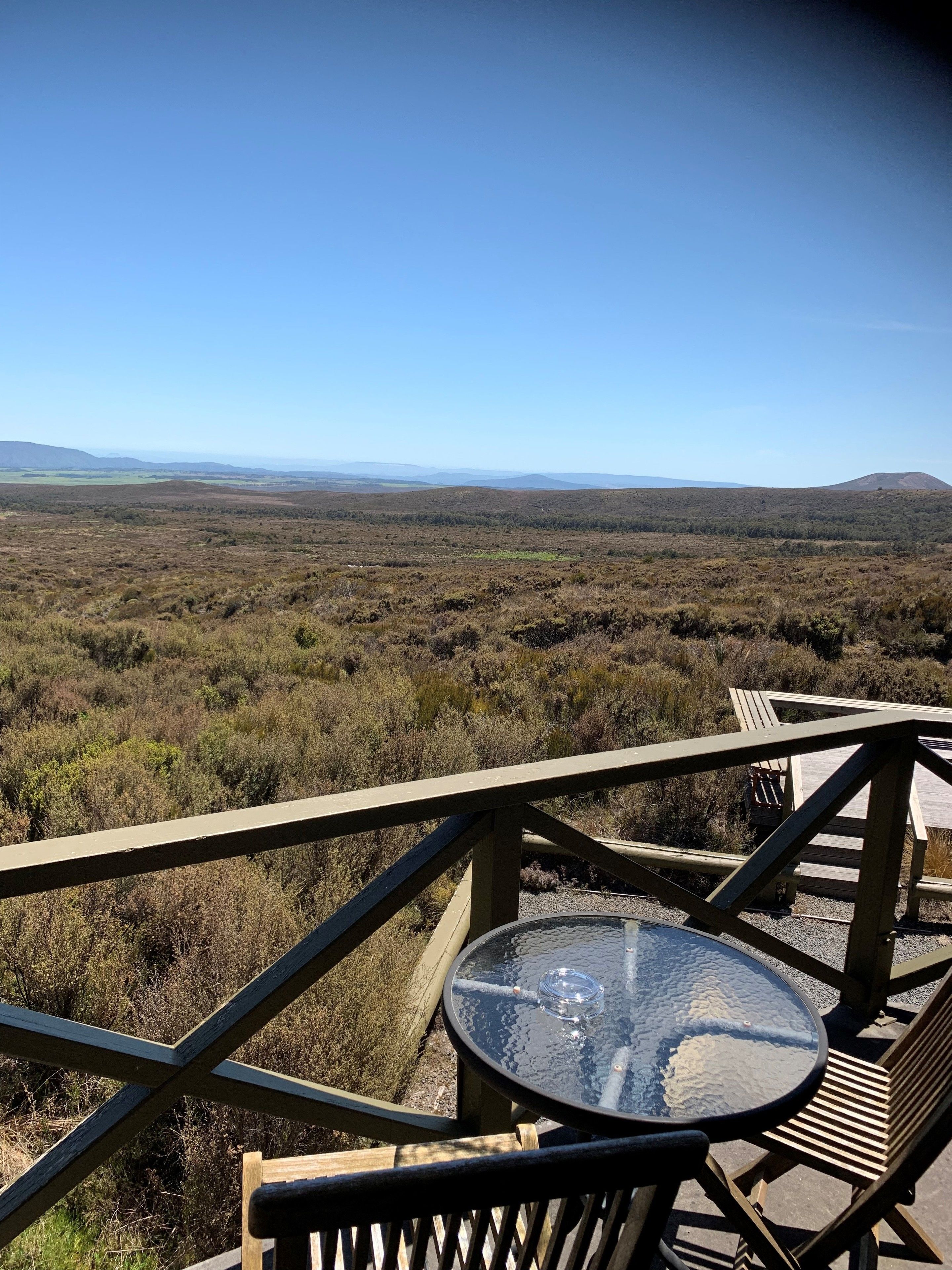 A deck with a glass table and chairs overlooking a vast, open landscape with distant hills.