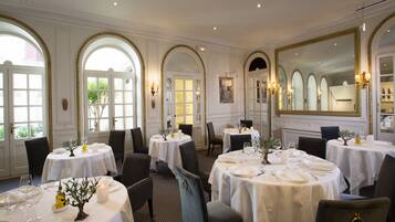 Une salle à manger élégante, avec plusieurs tables dressées pour le service, de grandes fenêtres en arc de cercle et un grand miroir.