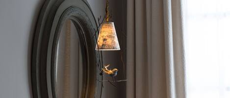 A wall with a large, oval mirror and a hanging light fixture with a bird perched on it.