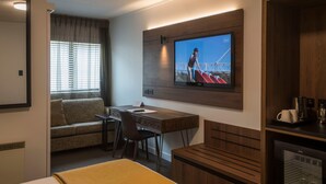 Una habitación de hotel con cama, escritorio, televisor, sofá y cafetera.