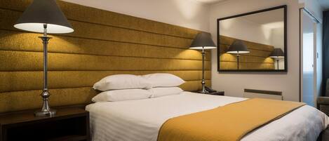 A hotel room with a large bed, two bedside lamps, a headboard with a textured pattern, a mirror on the wall, and a nightstand.