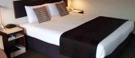 A hotel room with a large bed, a bedside table with a lamp, and a nightstand with a phone.