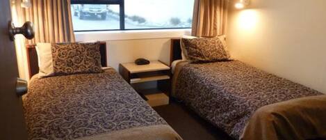 Habitación de hotel con dos camas individuales, una mesita de noche, una ventana con cortinas y una lámpara fijada a la pared.