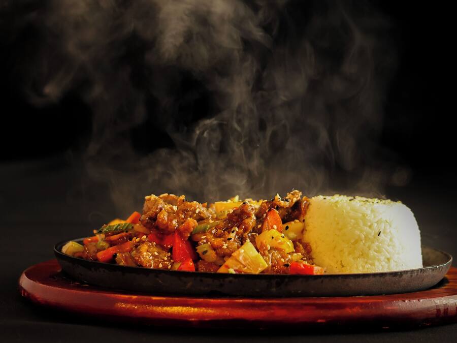 Un piatto di cibo con riso e carne, dal quale sale il vapore.