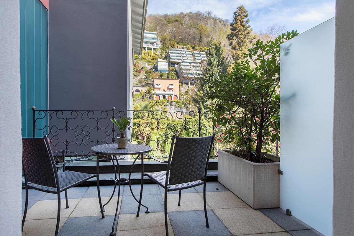 A balcony with two chairs and a table, a potted plant, and a view of buildings and trees.