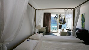 A hotel room with a bed, a desk, a chair, a small table, and a view of the sea. - Hotel Collinetta (Ascona)