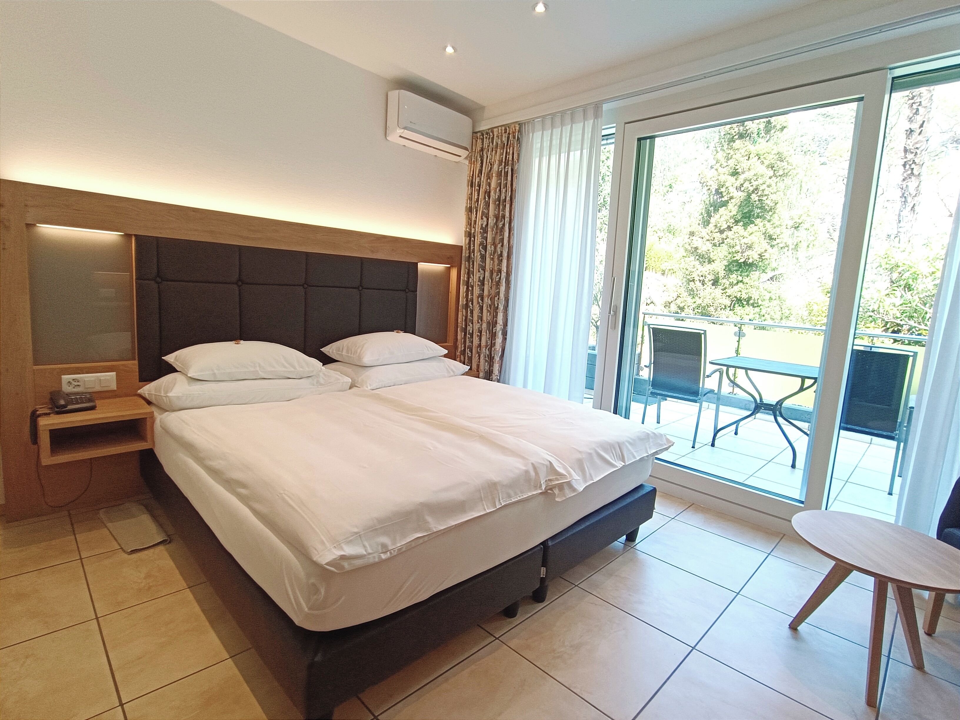 Una camera d'albergo con un letto grande, un comodino con il telefono e vista all'esterno tramite una porta scorrevole in vetro.