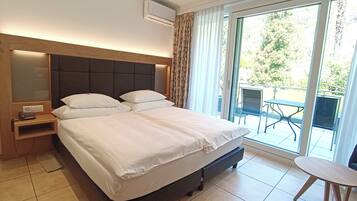 Una camera d'albergo con un letto grande, un comodino con il telefono e vista all'esterno tramite una porta scorrevole in vetro.