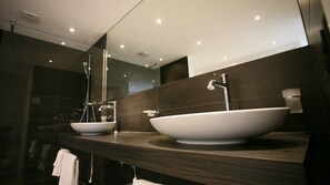 A modern bathroom with two sinks, a large mirror, and dark tiled walls.