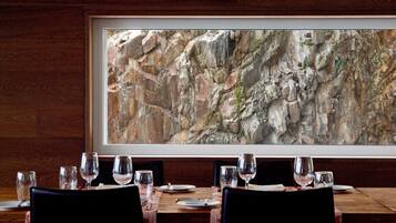 A dining area with a table set for four, a framed artwork depicting a rocky landscape, and wooden paneling on the walls.