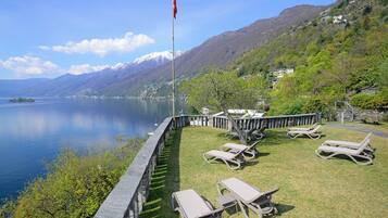Terraza junto al lago con sillones de descanso, una bandera y un muro de piedra con vistas a una montaña y un lago.