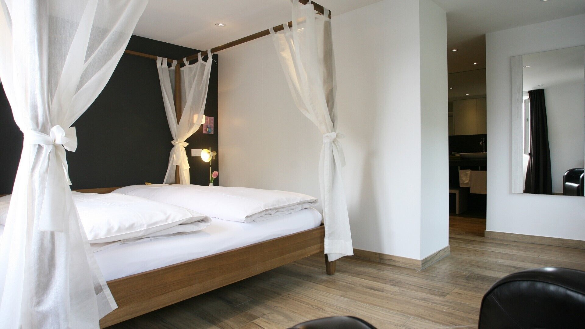 Een moderne slaapkamer met een houten bed, witte beddengoed en een hemelbed.