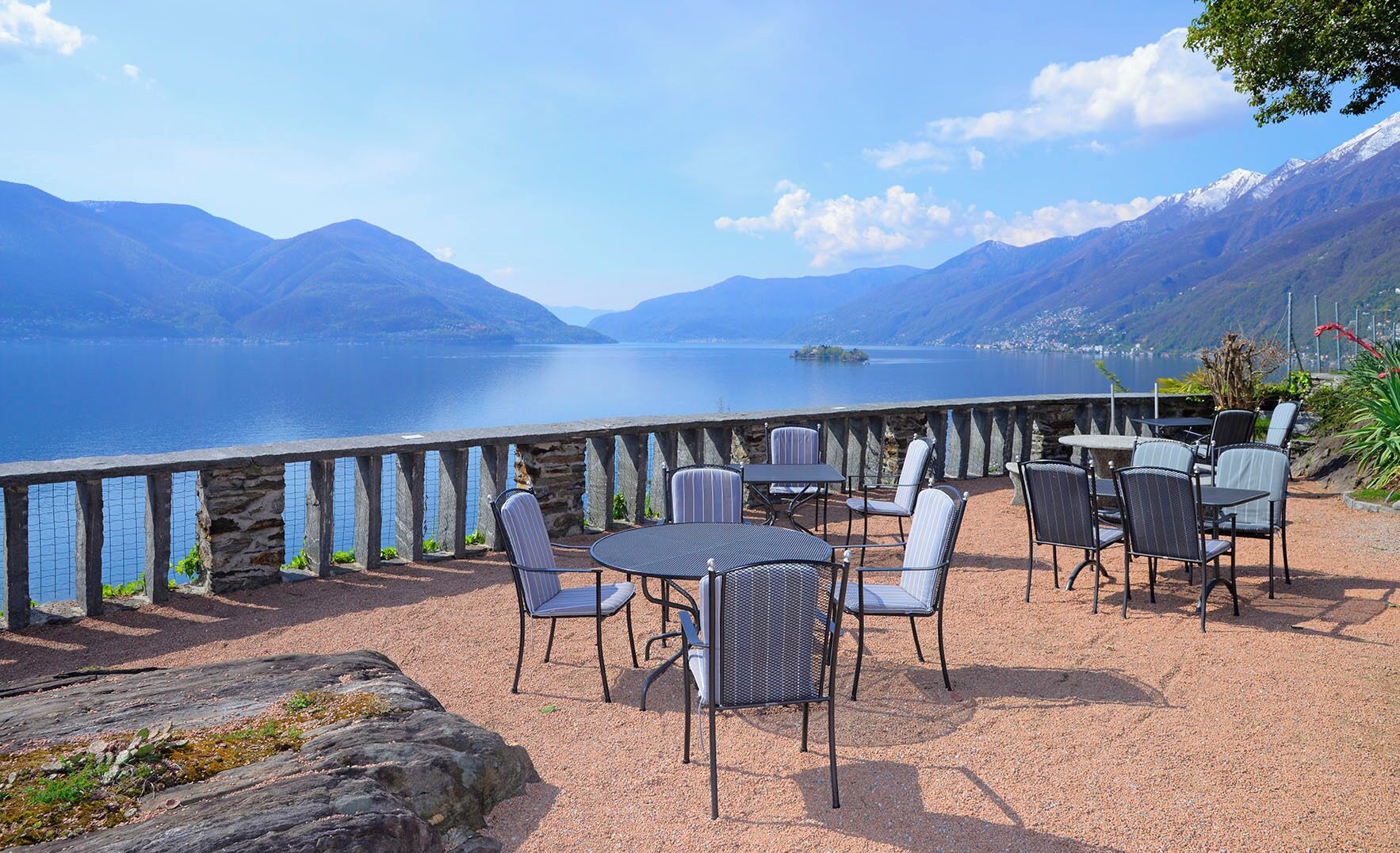 An outdoor seating area with tables and chairs overlooking a lake with mountains in the background.