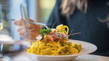 A plate of yellow pasta with shrimp and vegetables, held by a person.