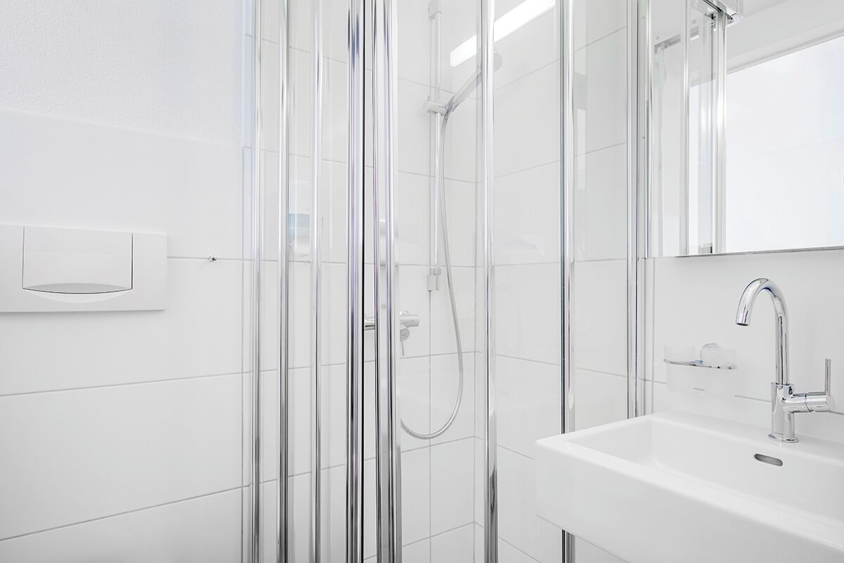 A modern bathroom with a glass shower enclosure, a white sink, and a mirror.