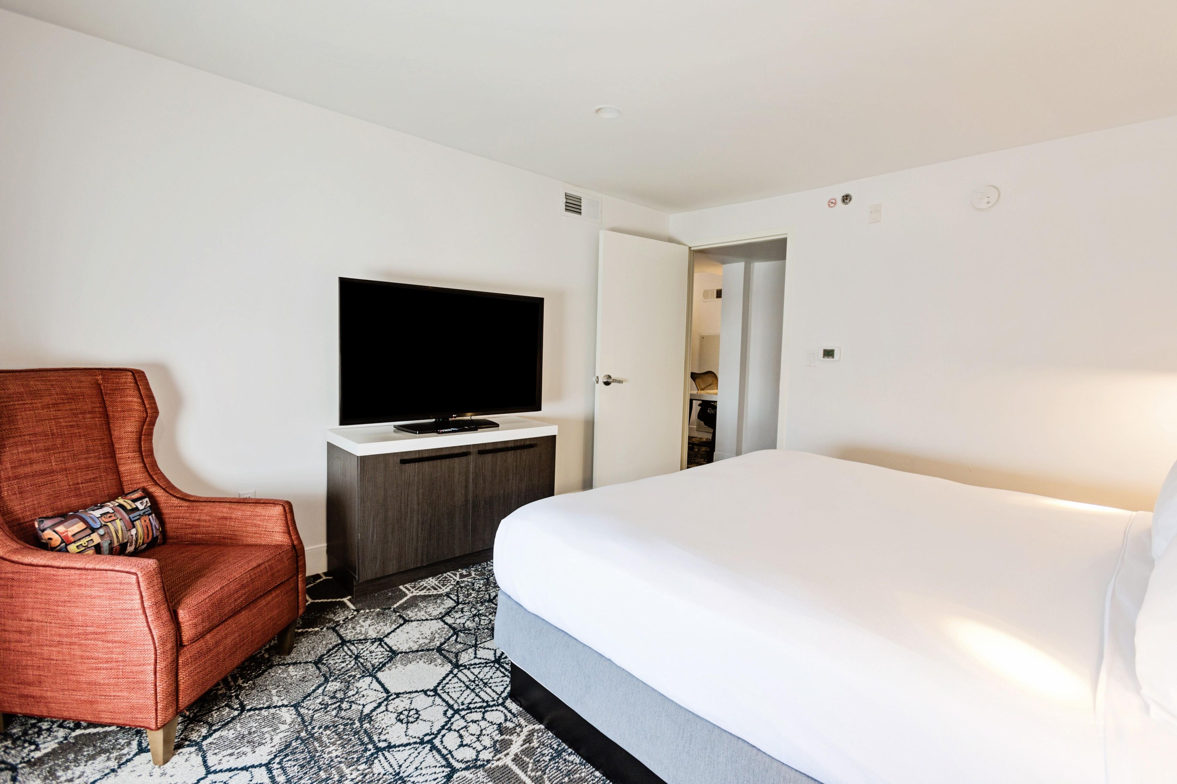 A hotel room with a bed, a television on a stand, a chair, and a wardrobe.