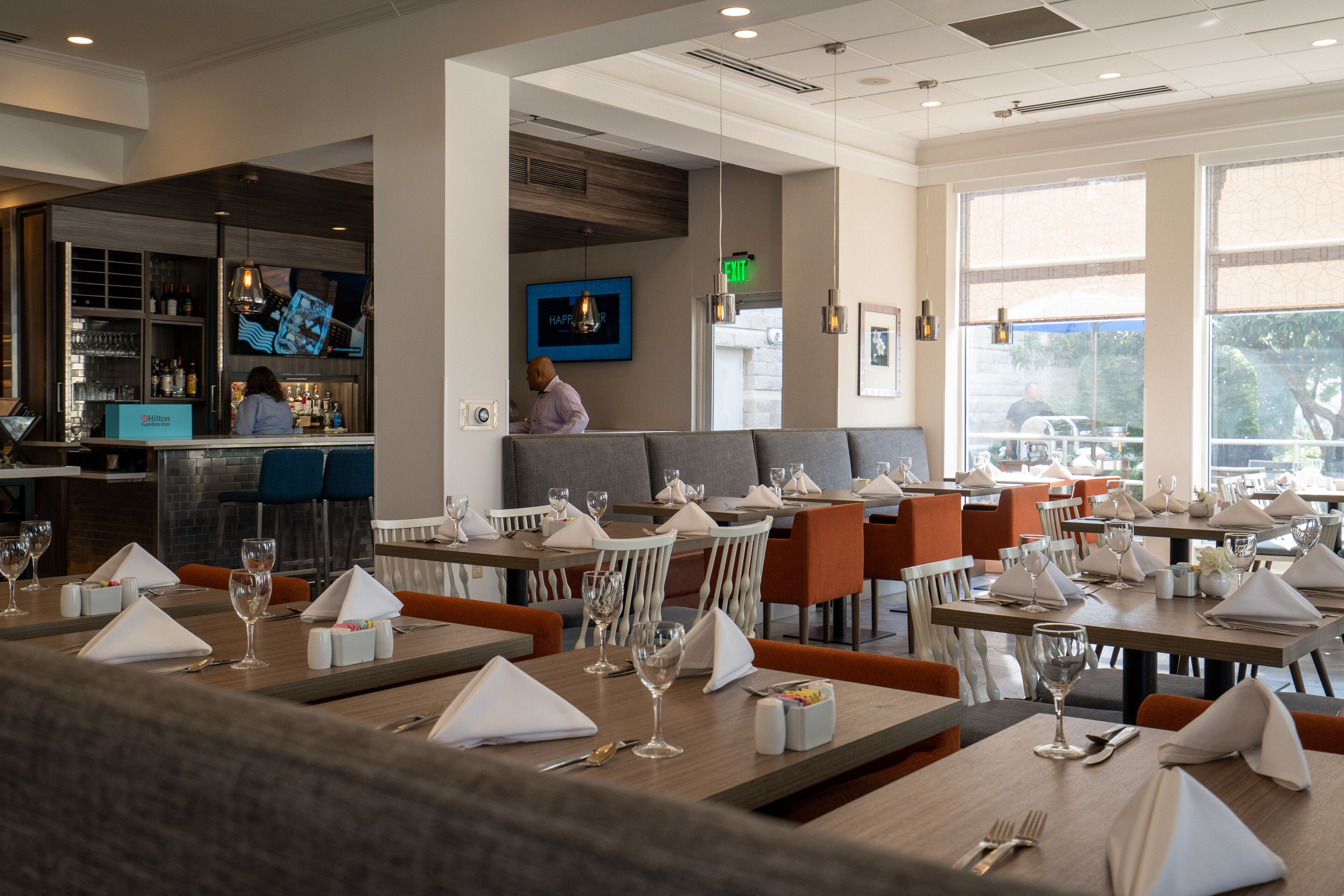 Een restaurant met keurig geordende tafels, een bar en een barista die drankjes klaarmaakt.