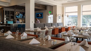 A restaurant with neatly arranged tables, a bar area, and a barista preparing drinks.