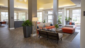 A spacious lobby with a large seating area, a reception desk, and large windows providing natural light.
