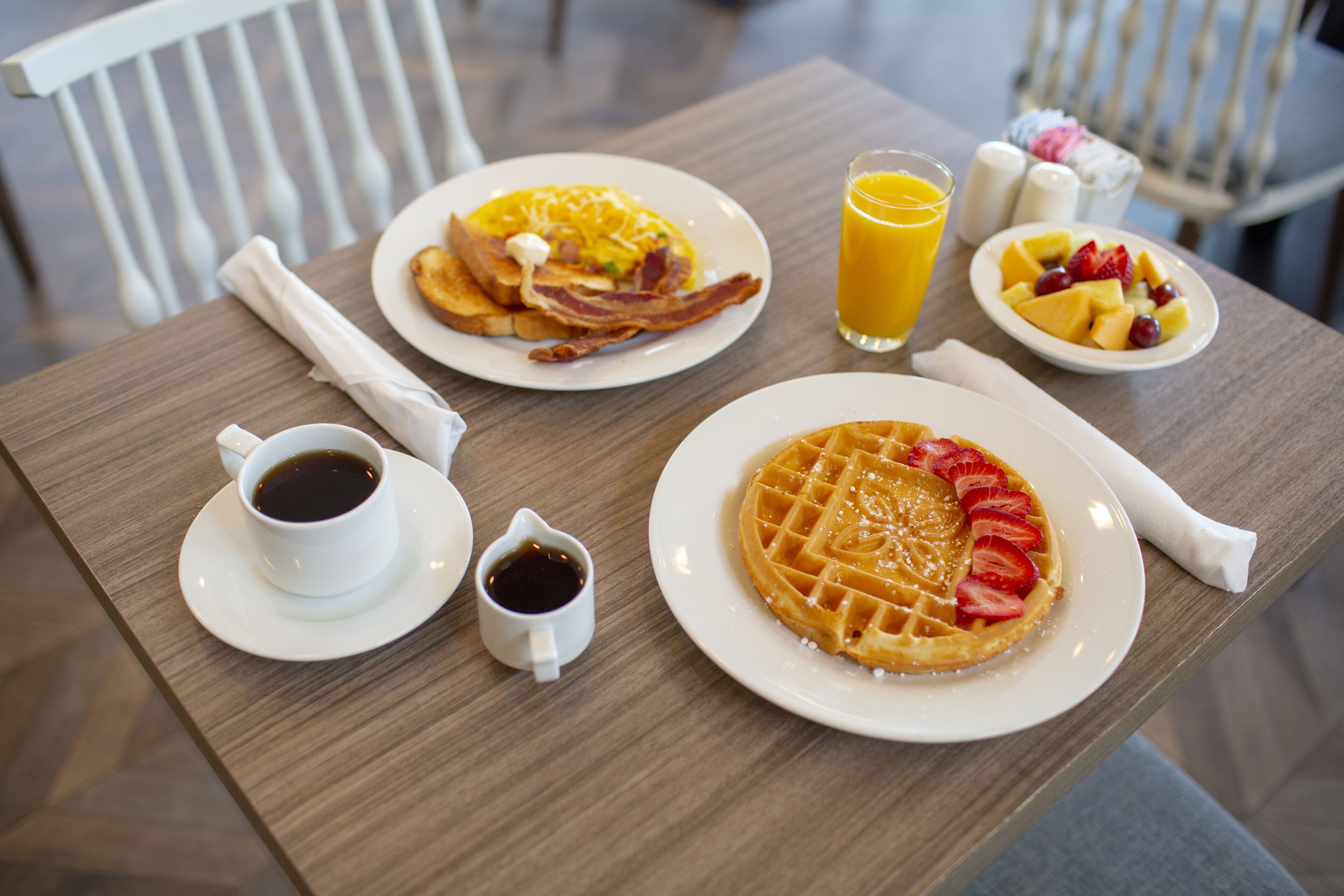 A breakfast table with plates of food, a cup of coffee, and a glass of orange juice.