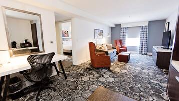 A hotel room with a desk, chair, sofa, and television.
