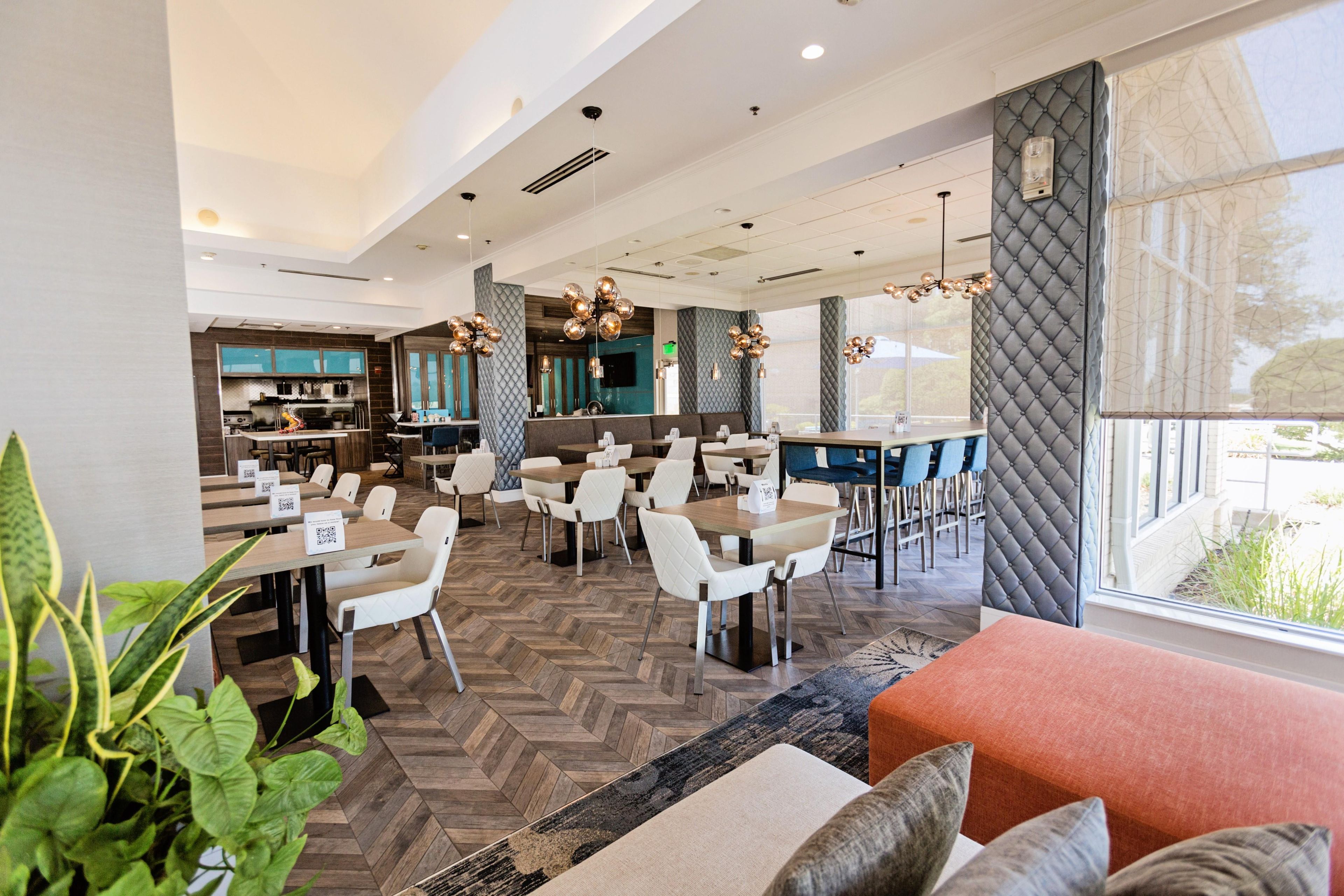 Un restaurante moderno con suelo de espiga, sillas blancas y una zona de bar.
