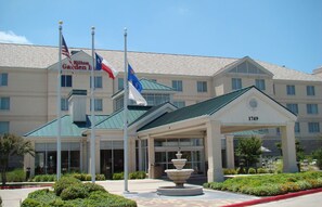 A hotel with a green roof, a fountain in front, and flags on flagpoles.