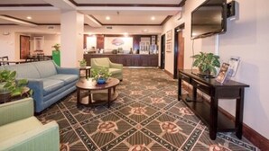 Un hall d’hôtel avec un tapis à motifs, un canapé, une table basse et un téléviseur fixé au mur.