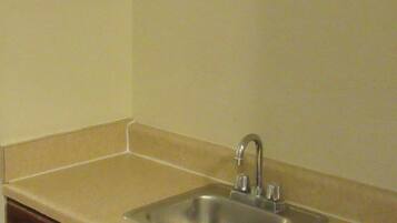 A kitchen with a stainless steel sink, beige countertop, and wooden cabinets.